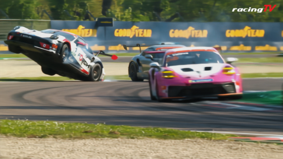 Two race cars on a curving track, one white with red accents lifting off the ground as the other pink car follows, Goodyear banners behind them.