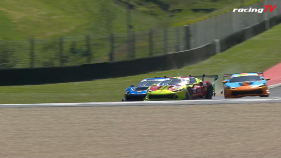 Three colorful race cars racing on a track with a safety barrier and grassy slope, RacingTV logo top-right.
