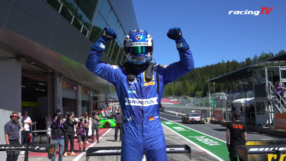 Race car driver in blue suit raises arms in victory on pit lane with cheering crew watching; 'racingTV' logo in top-right corner.