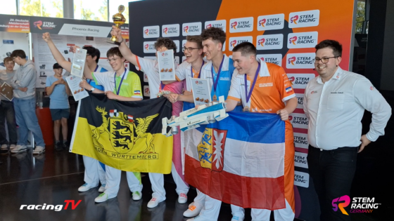 Group of young racers posing with state flags, medals, and a trophy after a STEM Racing event on a branded backdrop.