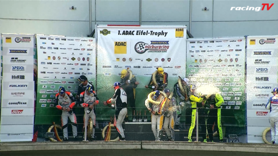 Winners on a podium spraying champagne amid sponsor banners at the ADAC Nürburgring event, RacingTV logo in top right.