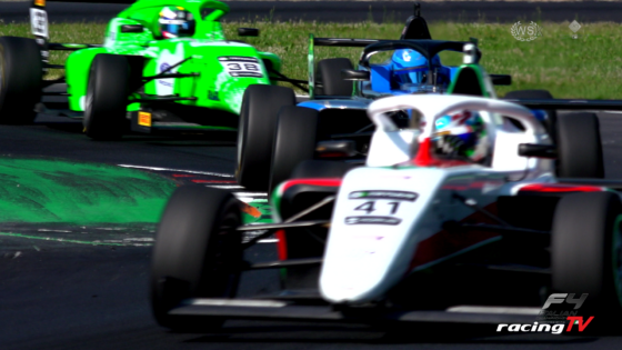 Open-wheel race cars in a tight bend: white car #41 leading, blue car behind, and bright green car further back on a track with grass beside it.