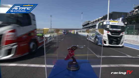 Driver's point-of-view on a truck racing pit lane with multiple trucks lined up and grandstands in the background, Goodyear FIA European Truck Racing Championship banner in the top-left corner