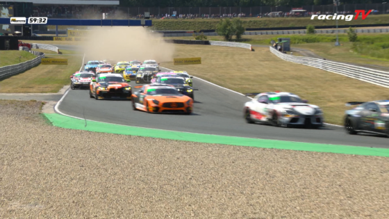 Group of colorful race cars speeding around a track with dust rising behind them on a sunny day, in a tight corner.