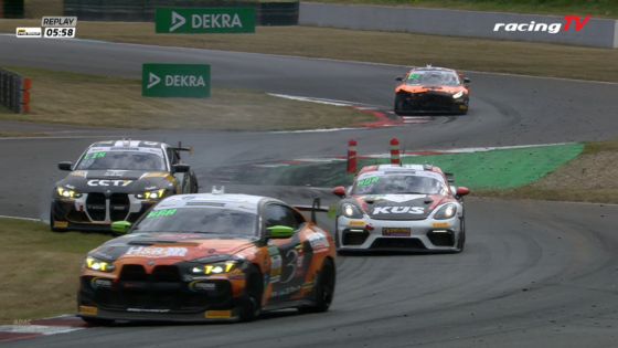 Race cars navigate a left-hand bend on a track, with an orange front car leading and others close behind.